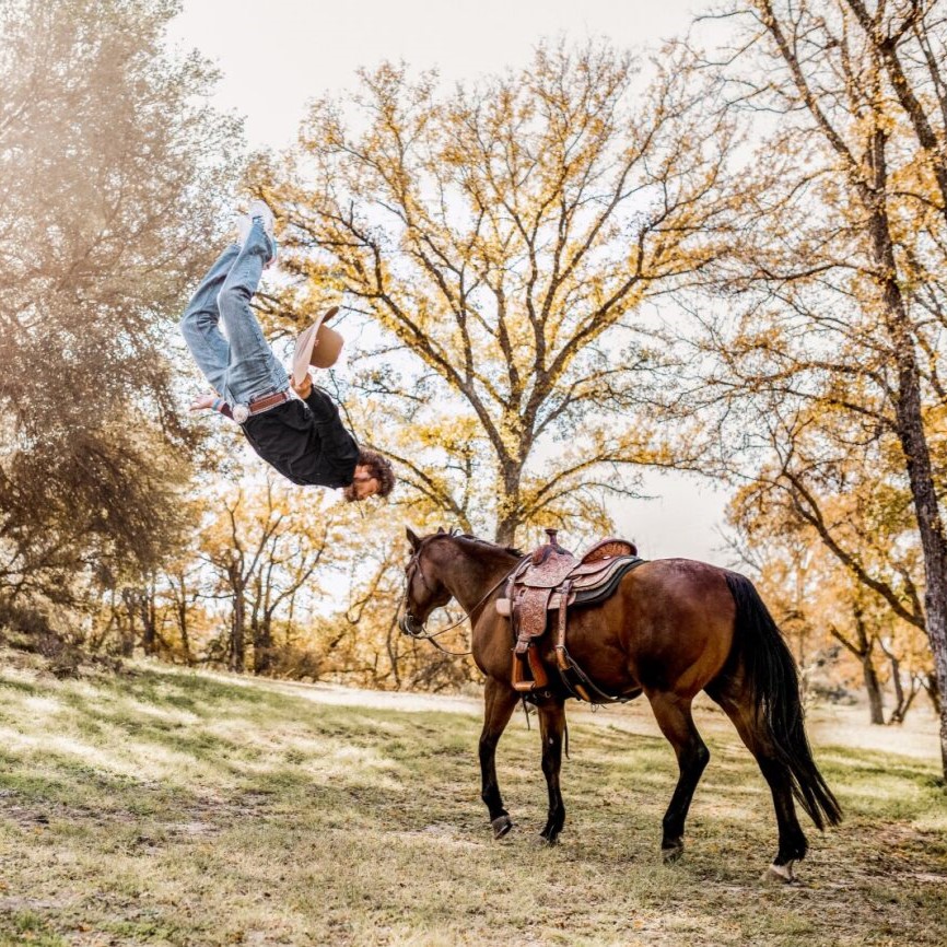 Cowboy doing a backflip in the forest and horse with saddle on
